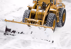 Gelber Schneepflug schiebt Schnee auf einer weiß bedeckten Oberfläche.